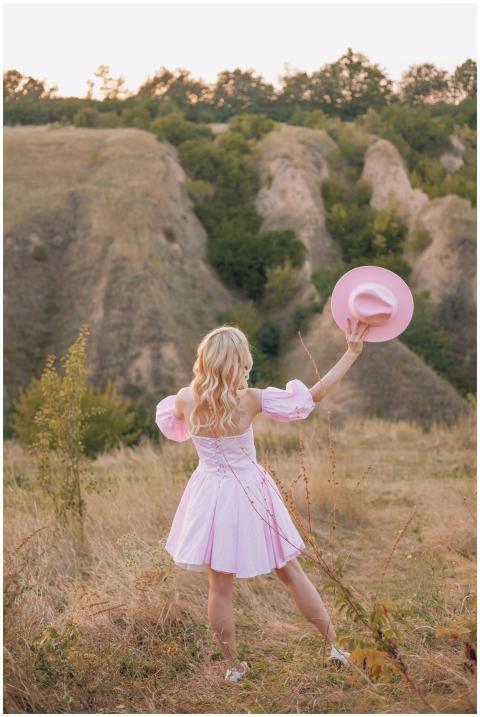 A blonde woman in a pink dress holding a hat stand