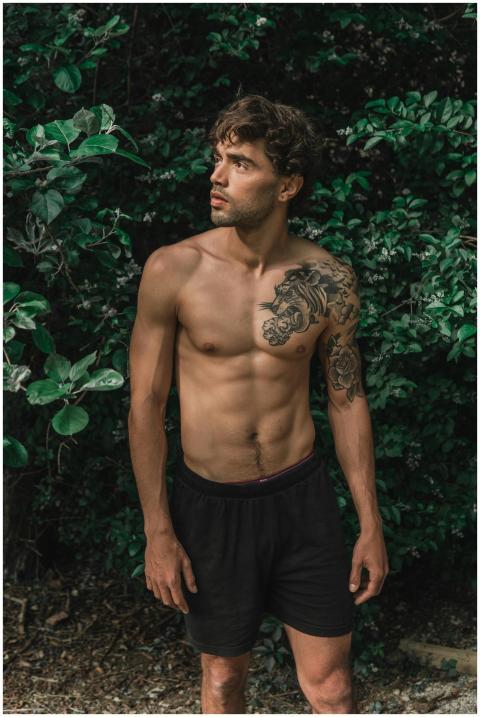 Shirtless man with tattoos posing amidst lush gree