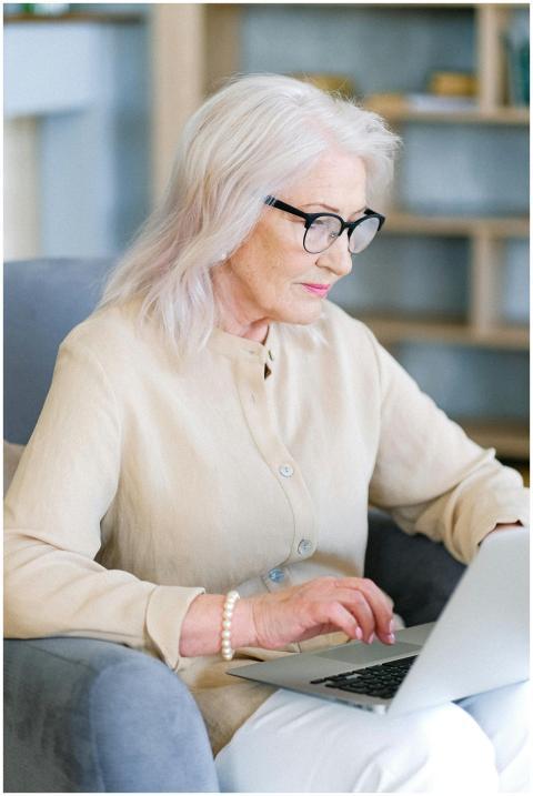 Elderly woman with glasses typing on a laptop in a
