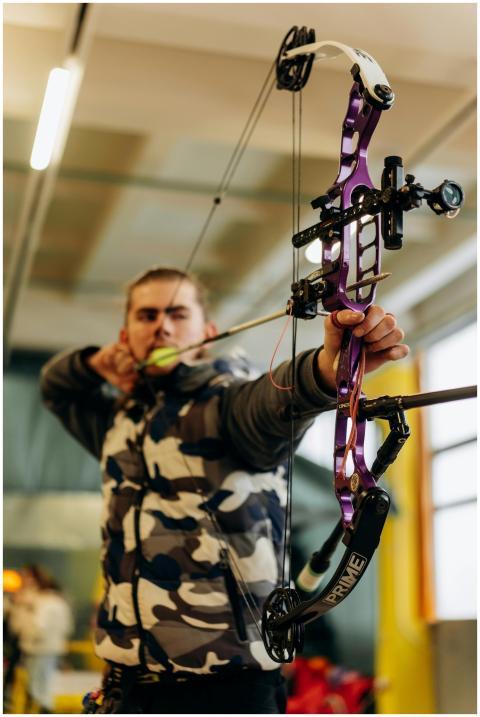 A man intensely focuses on aiming a purple compoun