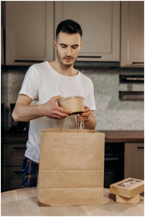 A young man in a kitchen packing takeout food into