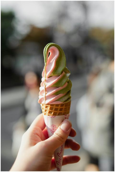 A hand holding swirled matcha and strawberry ice c