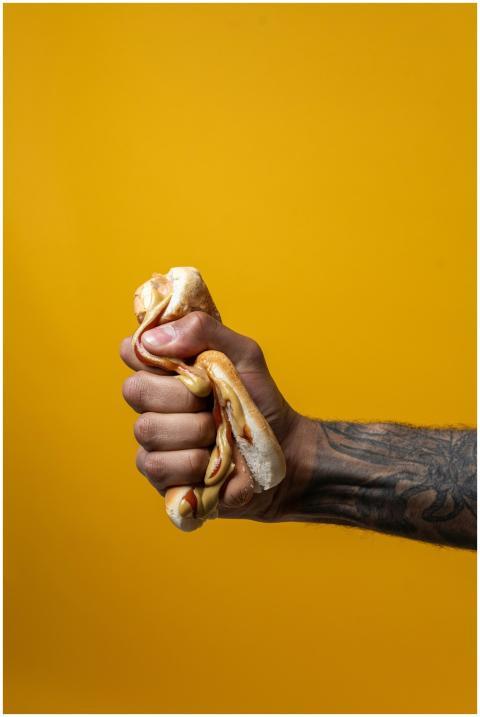 A hand squashes a hotdog, emphasizing dieting and