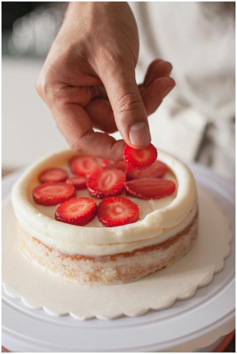 Close-up of hand decorating a cake with fresh stra