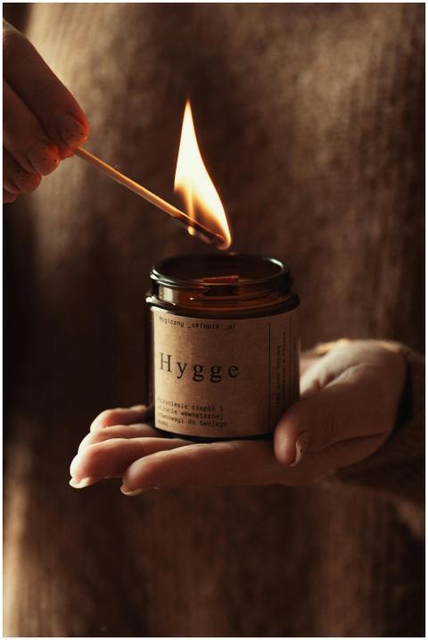 A hand lights a Hygge candle, creating a warm and