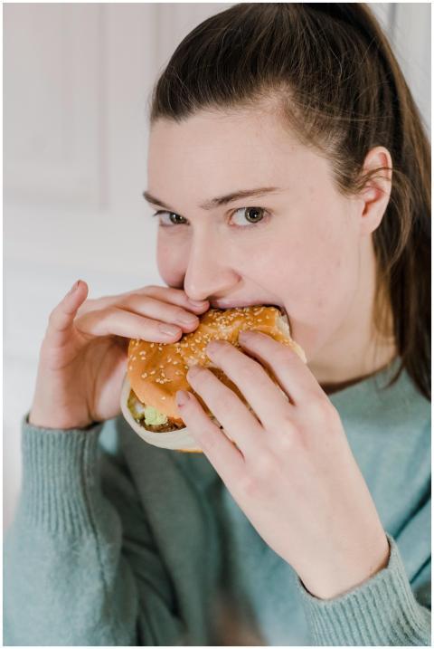 Young woman in a blue sweater taking a bite of a f