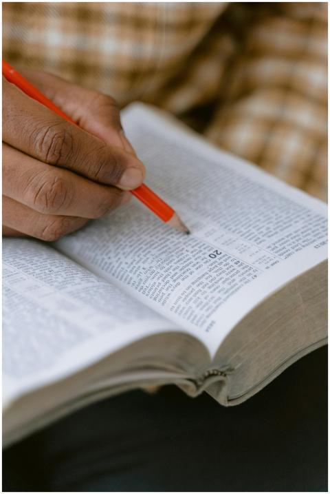 A hand holding a pencil marks text in an open holy