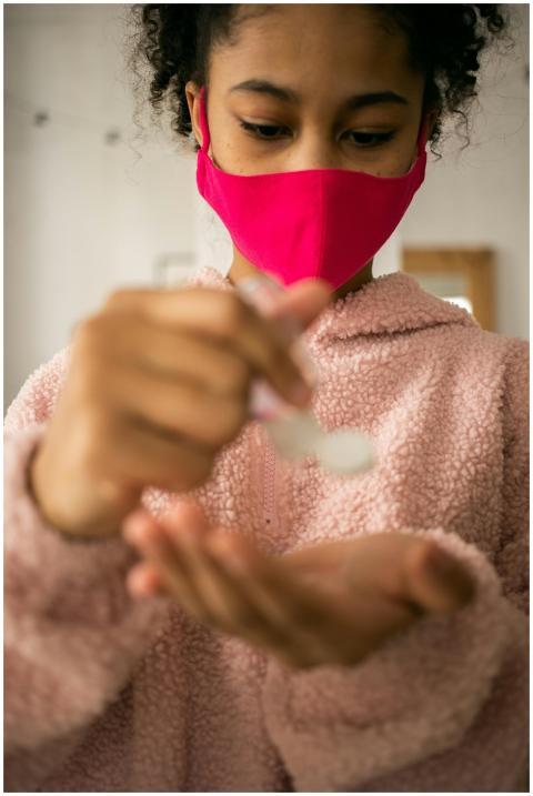 A teenage girl in a pink mask applying sanitizer a