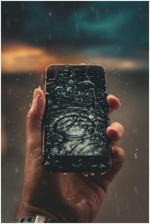 A person holds a smartphone with raindrops on scre