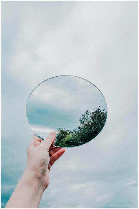 A hand holding a circular mirror reflecting a part