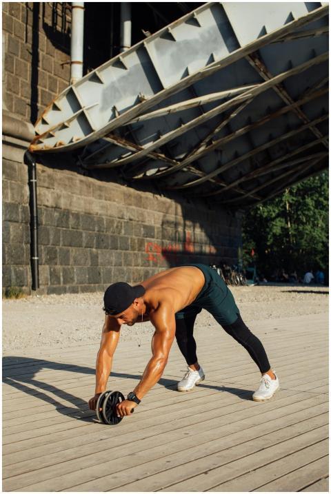 Fit man using ab roller under a bridge for an outd