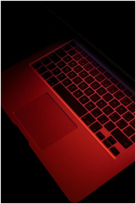 Close-up of a laptop keyboard under red lighting,