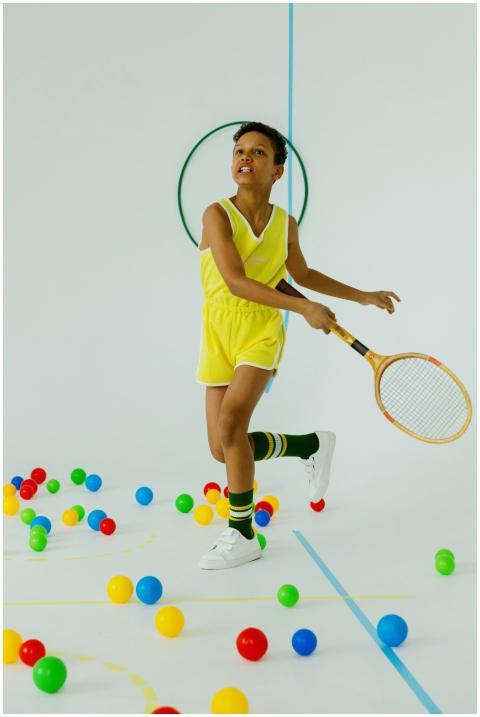 Child in sportswear playing tennis indoors with co