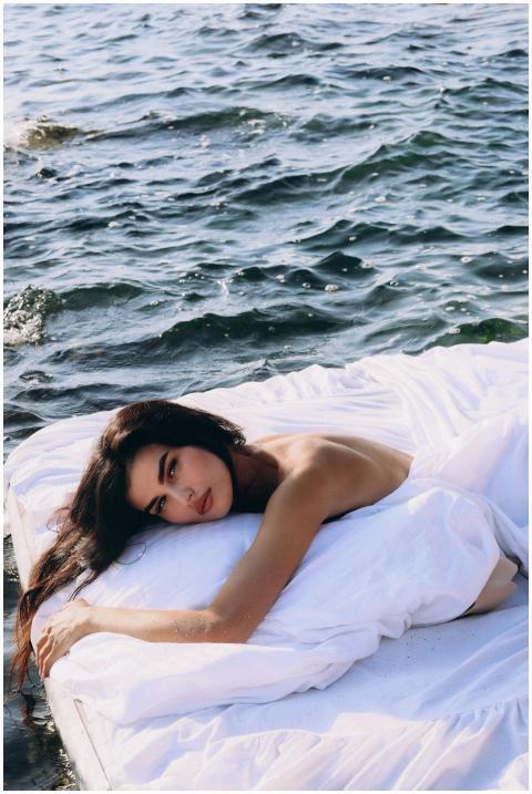 A woman on a white mattress floating on calm sea w