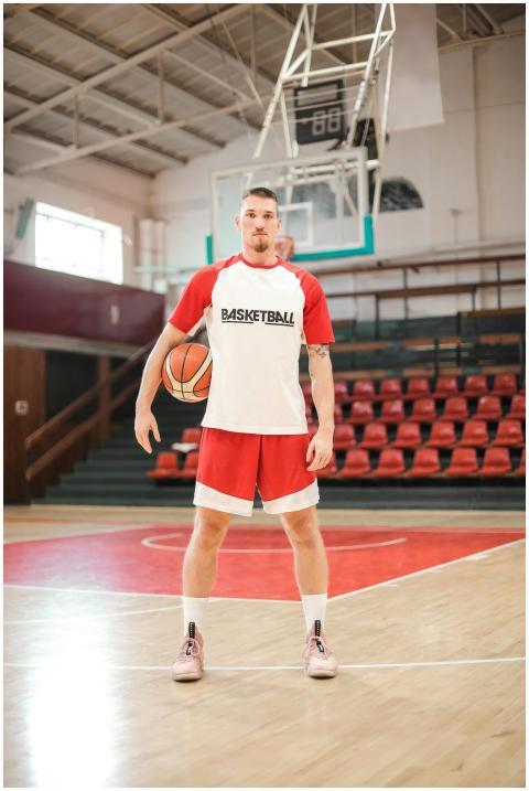 A basketball player poses on an indoor court, read