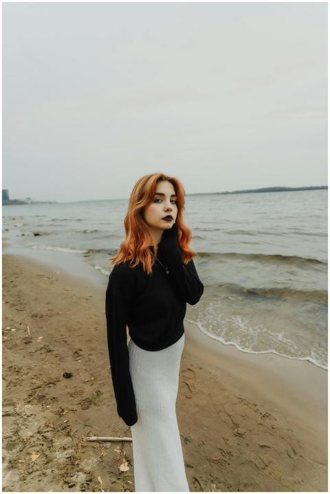 Woman with red hair on a sandy beach wearing a bla
