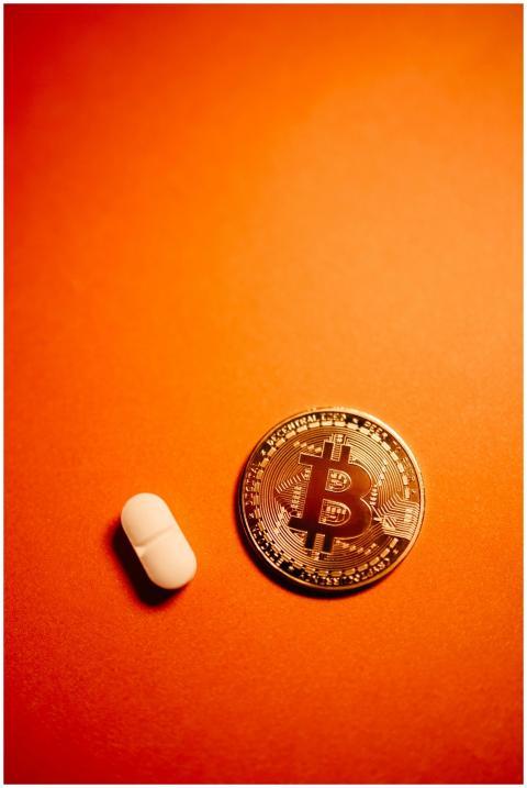 Bitcoin coin next to a pill on an orange backgroun