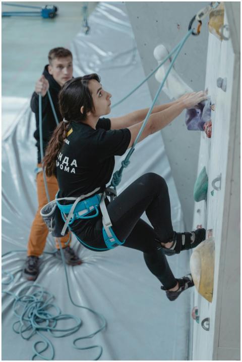 A woman harnessed for safety climbs a rock wall in