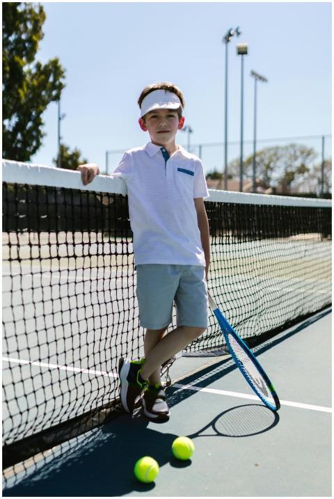 A young boy poses with a tennis racket on an outdo