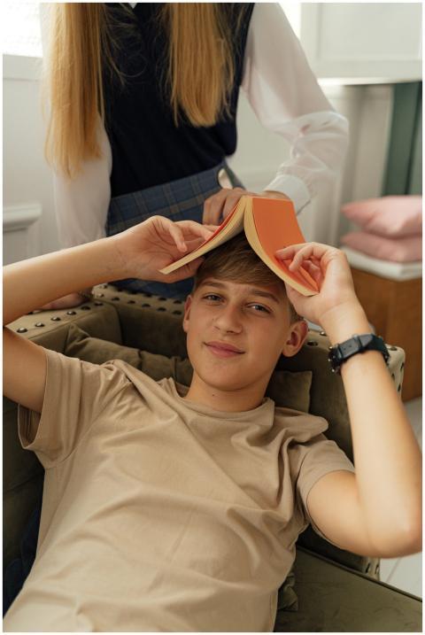 Caucasian teen boy smiling with book on head indoo