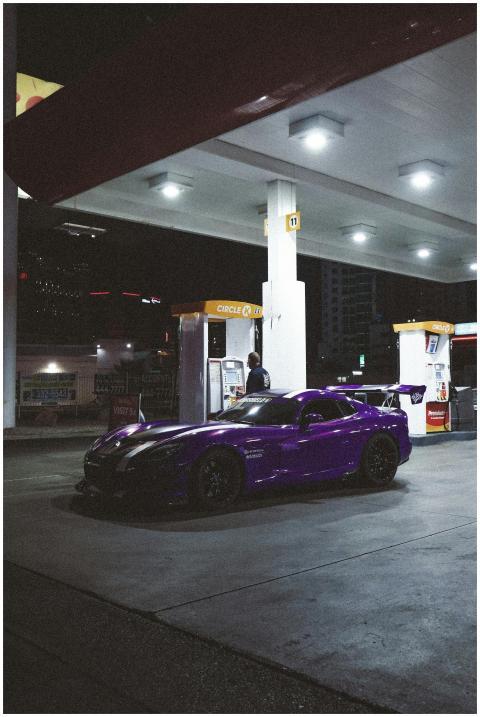 A sleek purple sports car at a gas station under b