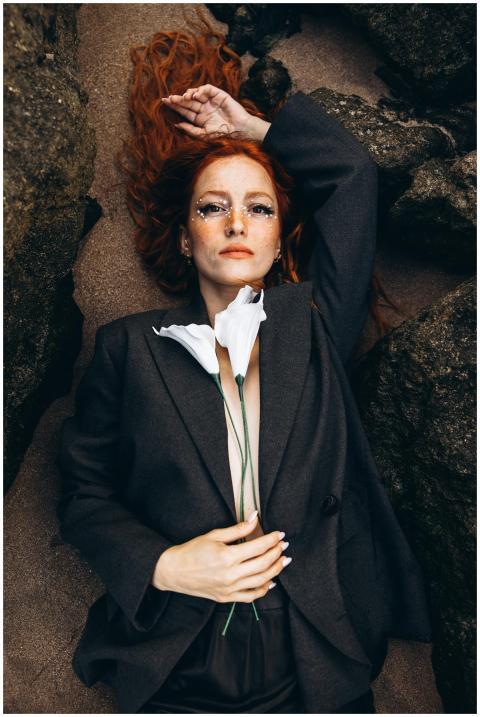 Creative portrait of a woman lying among rocks, ho