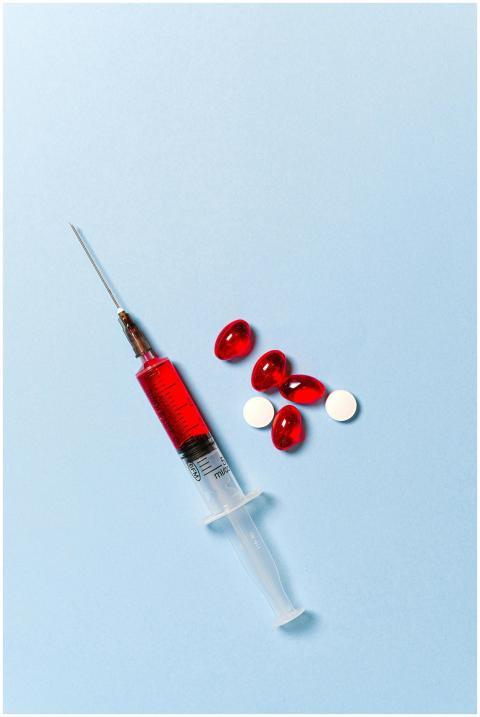 Syringe with red liquid and pills on a blue backdr