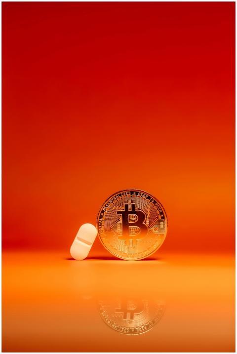 A bitcoin coin and white pill on a vivid orange ba