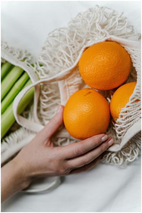 A hand places oranges into a reusable mesh bag, em