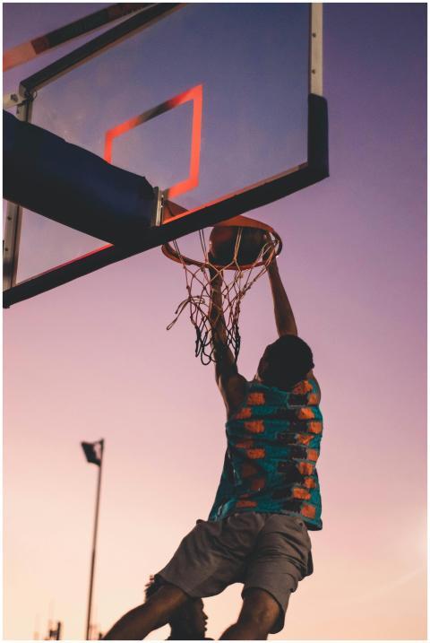 A basketball player successfully dunks as the sun