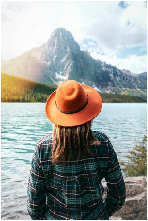 A woman in a fedora enjoys a serene view of a moun