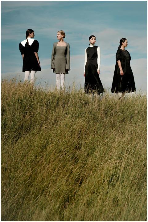 Four women in simple dresses standing on a grassy