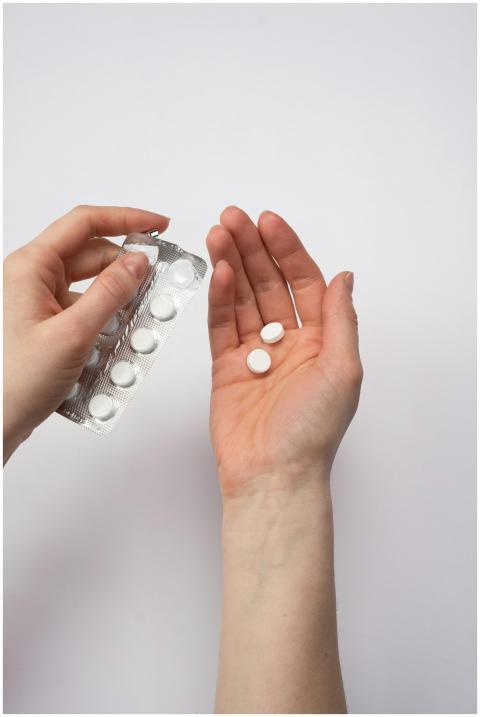 A person's hands holding white pills, symbolizing