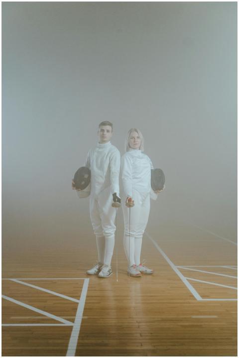 Two fencers in foggy studio standing with swords,