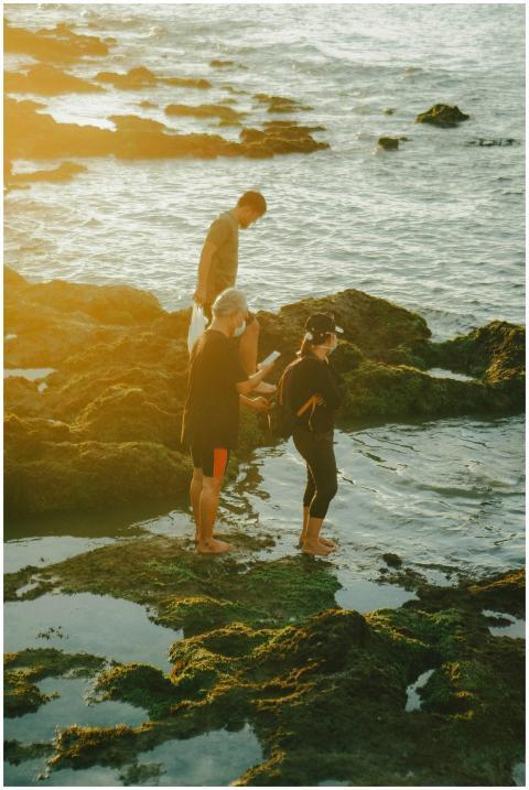 Three adults exploring rocky seashore during a war