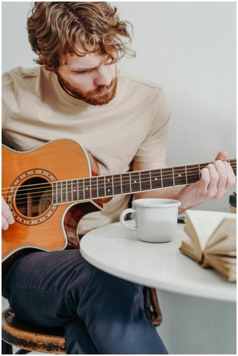 A young man strums acoustic guitar while sitting i