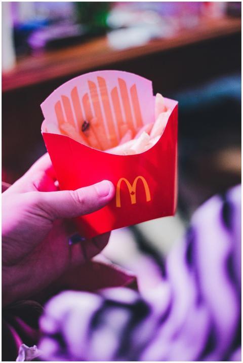 Hand holding a red fast-food box of french fries.