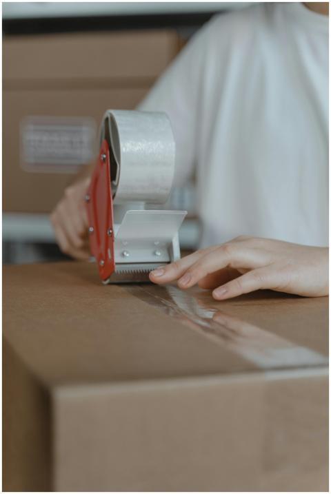 A person sealing a cardboard box with a tape dispe