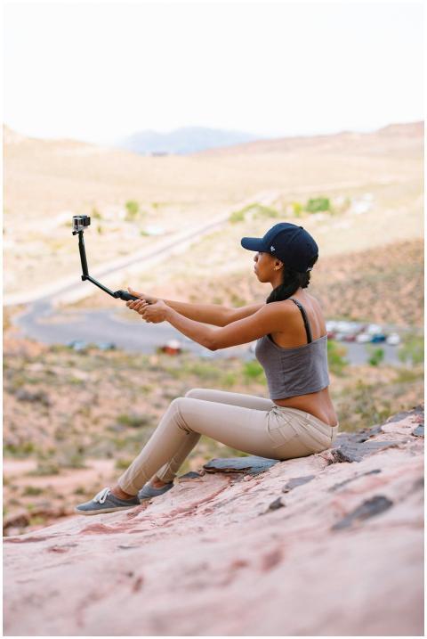 A woman sits on a rock vlogging with a camera amid