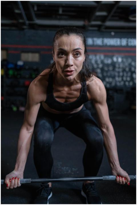 Focused woman lifting a barbell in a gym setting,