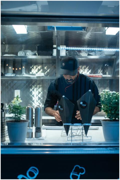 Man in food truck wearing a black cap and uniform,
