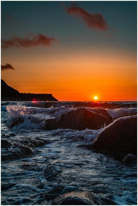 Dramatic sunset over ocean waves crashing onto roc