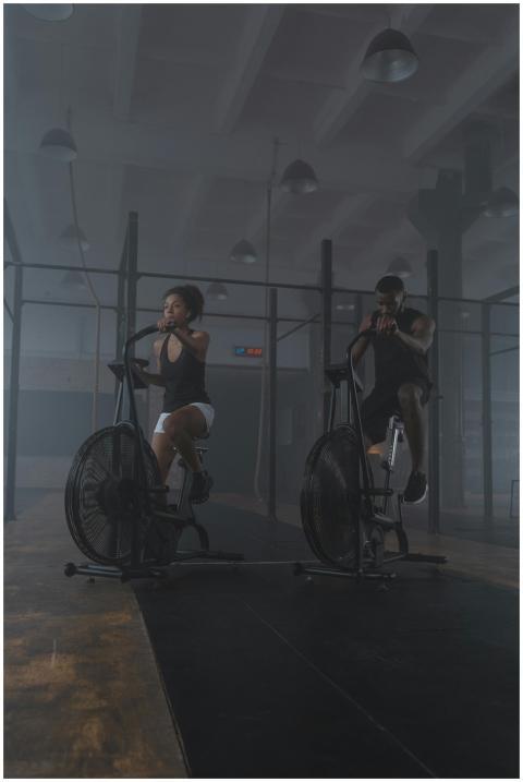 A focused pair of athletes exercising on air bikes