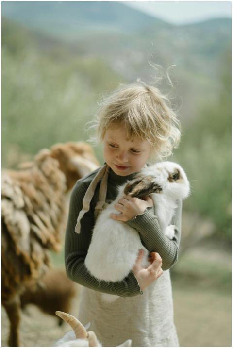 Blond child gently holding a white rabbit outdoors