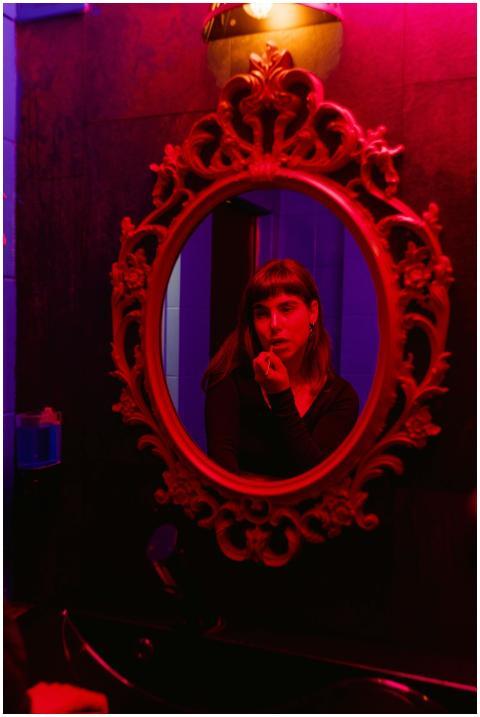 A woman applies makeup in a dimly lit room with an