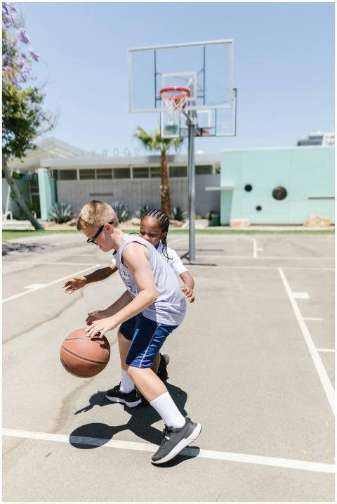 Two kids playing basketball on an outdoor court on