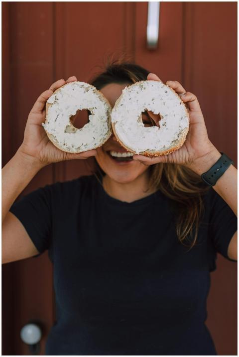 Smiling woman holding bagels with cream cheese pla