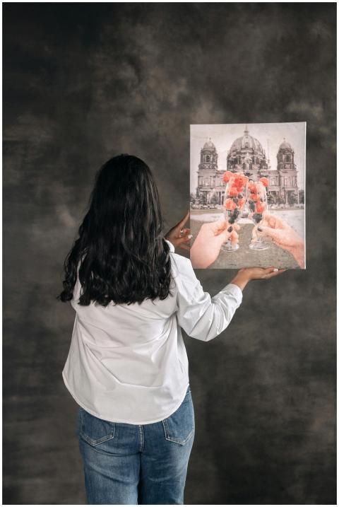 A woman in casual attire holds a painting featurin