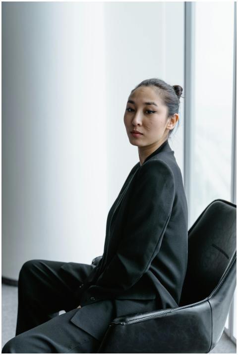 Confident woman in black blazer sitting indoors lo