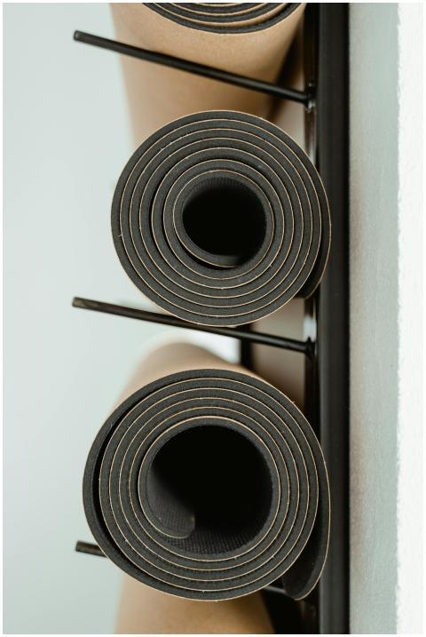 Rolled yoga mats neatly stacked on a rack indoors,